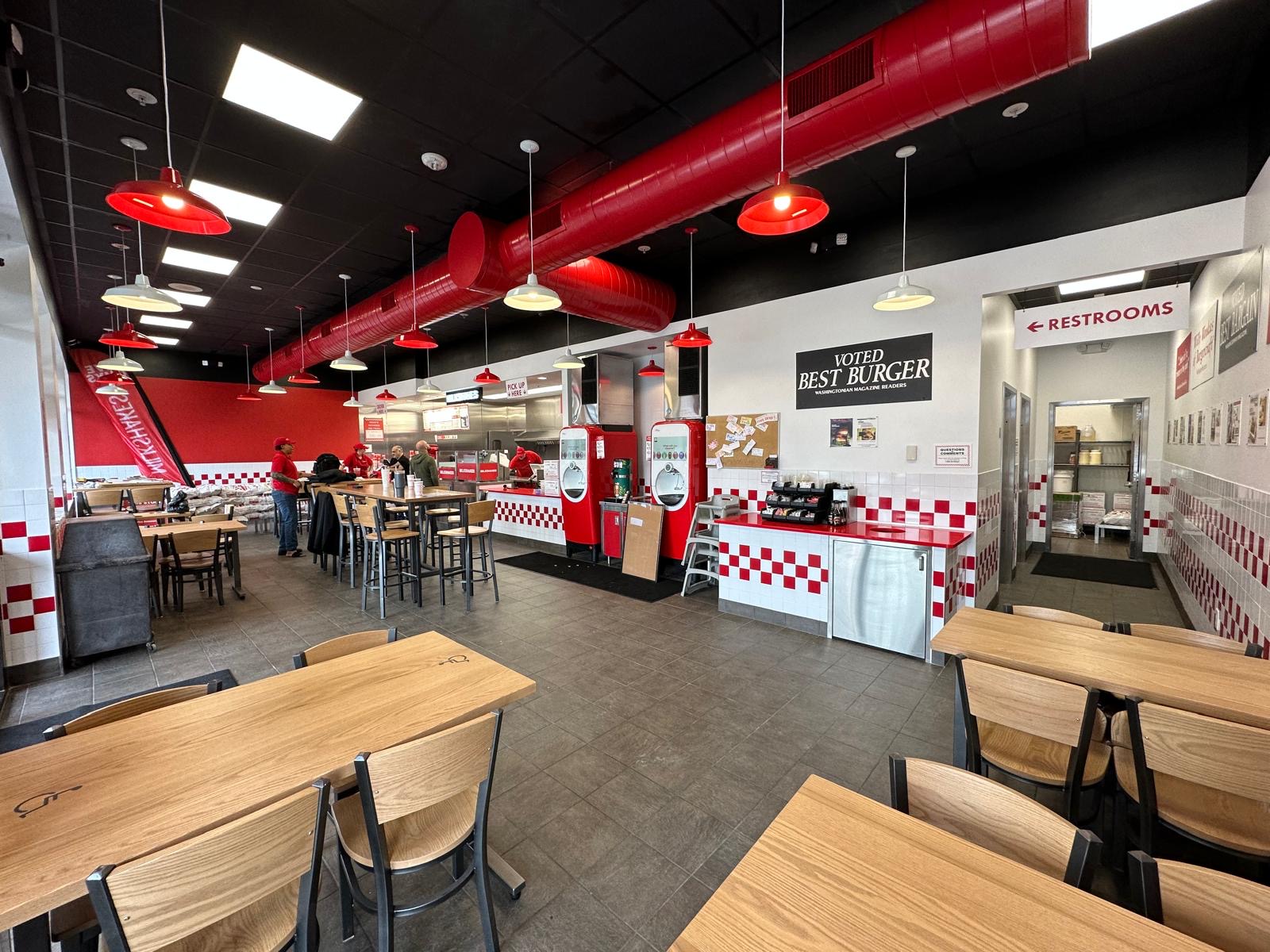 Finished Five Guys dining room with red pendant lights, exposed ductwork, and red-and-white checkered tile
